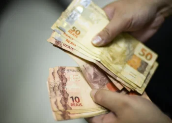 "Foto de mãos segurando cédulas de 10 e 50 reais, representando um pagamento."