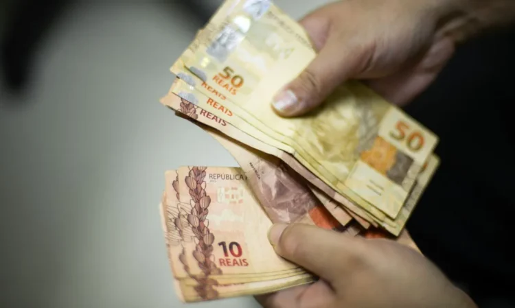 "Foto de mãos segurando cédulas de 10 e 50 reais, representando um pagamento."