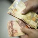 "Foto de mãos segurando cédulas de 10 e 50 reais, representando um pagamento."
