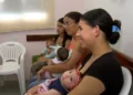 Mães sentadas em sala de espera, cada uma segurando um bebê nos braços.