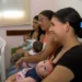 Mães sentadas em sala de espera, cada uma segurando um bebê nos braços.