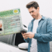 Homem conferindo celular com carteira de habilitação brasileira em destaque ao lado de carro branco