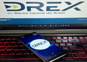 "Imagem de um celular exibindo o aplicativo DREX, com logo do Banco Central do Brasil ao fundo"