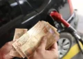 "Pessoa segurando cédulas de 50 reais enquanto abastece o carro, ilustrando os impactos das mudanças econômicas no cotidiano."