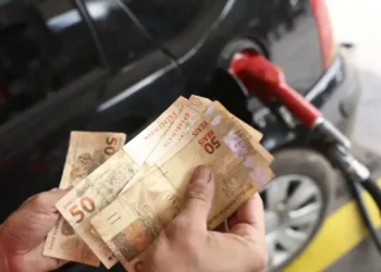 "Pessoa segurando cédulas de 50 reais enquanto abastece o carro, ilustrando os impactos das mudanças econômicas no cotidiano."