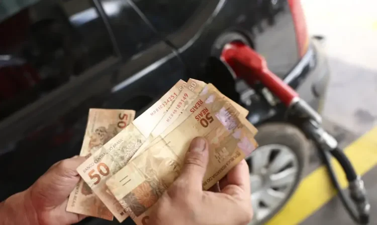 "Pessoa segurando cédulas de 50 reais enquanto abastece o carro, ilustrando os impactos das mudanças econômicas no cotidiano."