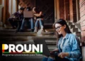 Estudante sorridente usando laptop nas escadas, ilustrando a novidade para prounistas sobre a possibilidade de acumular mais de um auxílio financeiro.