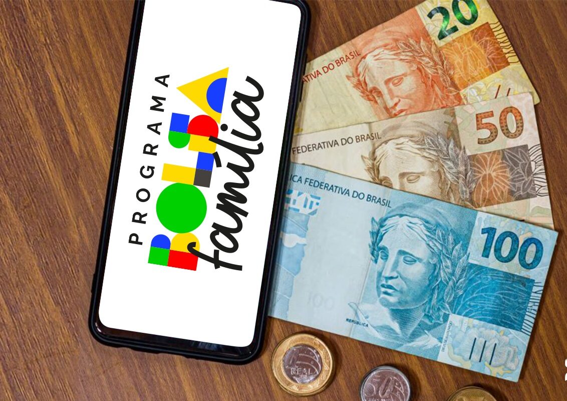 Aplicativo Bolsa Família aberto no celular ao lado de cédulas de reais sobre uma mesa.