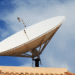 Antena parabólica digital instalada em telhado, com céu claro e nuvens.
