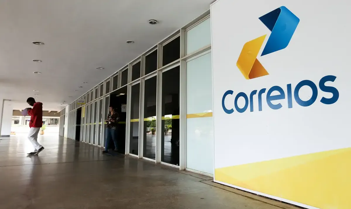 Fachada da agência dos Correios com pessoas entrando e saindo em dia claro