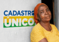 Mulher com blusa amarela e lenço vermelho, com expressão serena, ao lado de um mural com a logo do Cadastro Único, com foco na importância de atualizar dados para garantir o Auxílio Gás.