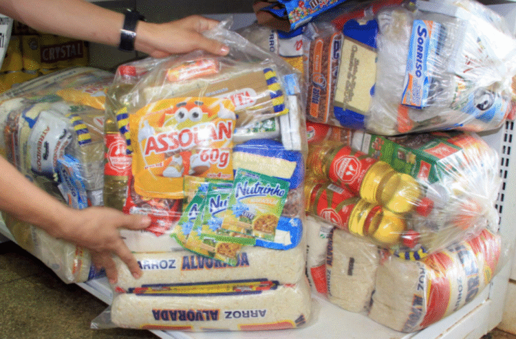 Imagem de cestas básicas sendo preparadas para distribuição, com produtos como arroz, óleo e macarrão.