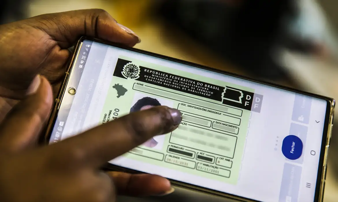 Pessoa segurando celular mostrando a carteira nacional de habilitação digital na tela