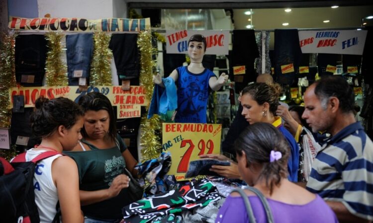 Clientes em frente a loja popular com promoções e roupas expostas