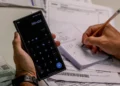 Pessoa utilizando calculadora e fazendo anotações enquanto calcula dívidas, simbolizando o esforço para negociar com o Serasa.