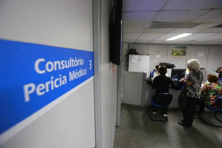 Consultório de perícia médica do INSS, com pessoas sendo atendidas para revisão de benefícios de auxílio-doença.