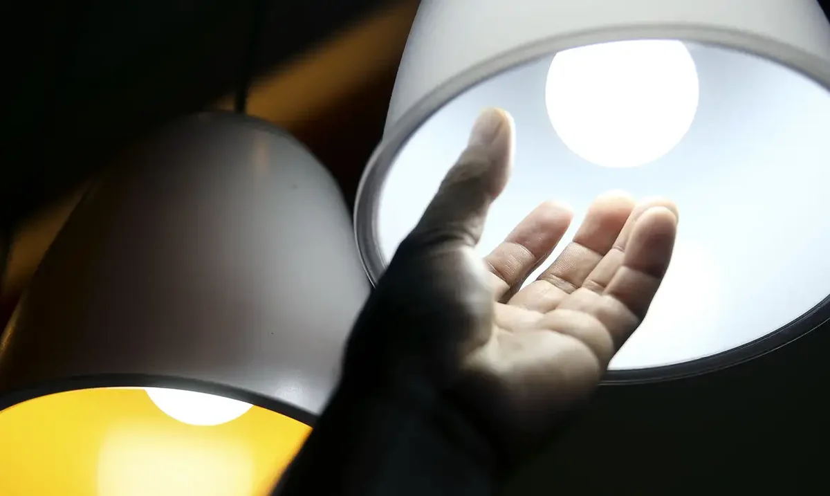 Mão se aproximando de lâmpada com luz branca, ilustrando a economia de energia com a conta de luz gratuita.