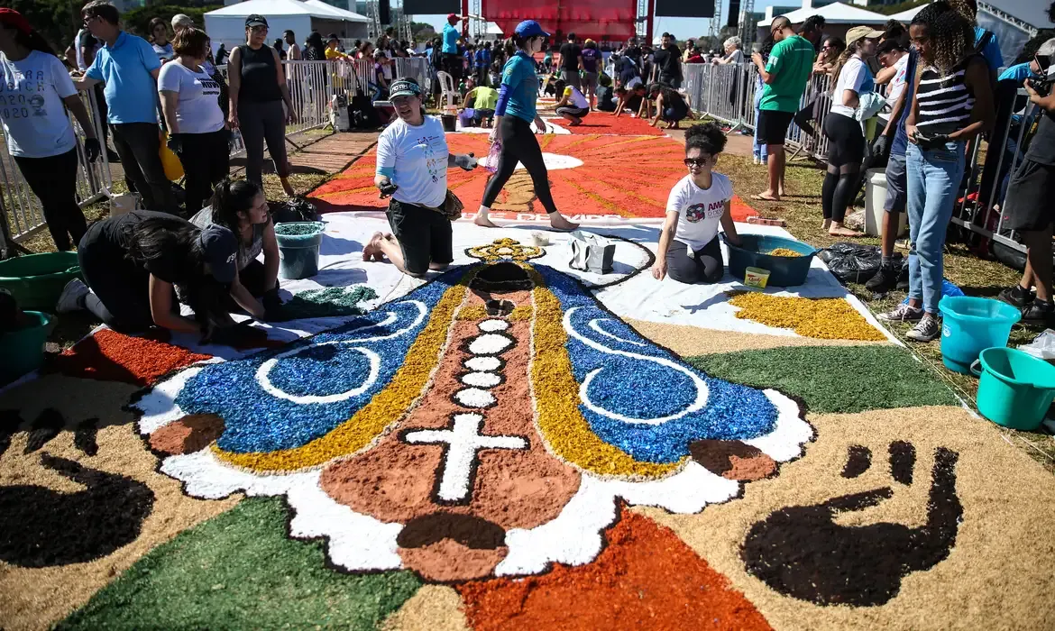 Participantes criando tapete de flores durante celebração do Corpus Christi, representando a imagem religiosa.