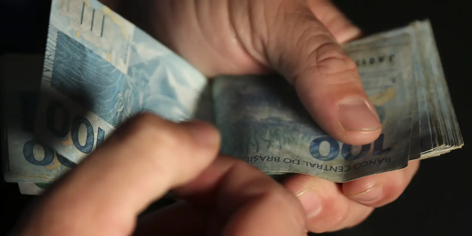Cédulas de 100 e 200 reais organizadas em leque sobre fundo preto