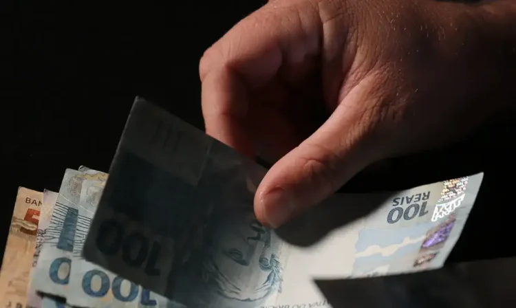 Pessoa segurando cédulas de R$ 100 e R$ 50, ilustrando a oportunidade de crédito para trabalhadores