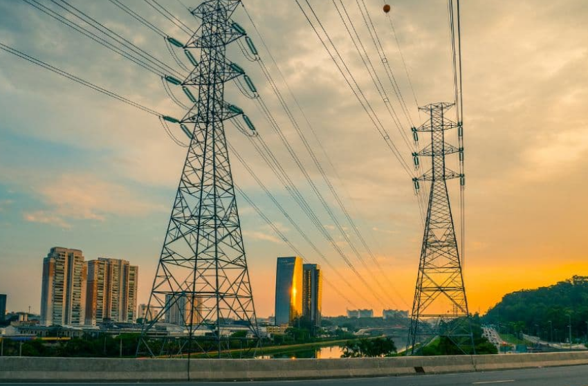 Linhas de transmissão de energia elétrica com prédios ao fundo, simbolizando a implementação da tarifa social de energia elétrica.