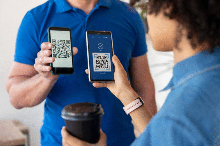 Dois smartphones exibindo QR codes, com uma pessoa segurando um café e outra escaneando o código, sugerindo o uso de IA para detectar fraudes em pagamentos.