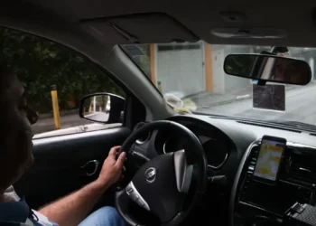 Motorista de aplicativo dirigindo veículo com aplicativo de corridas aberto no celular