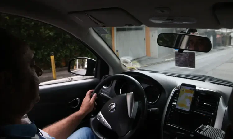 Motorista de aplicativo dirigindo veículo com aplicativo de corridas aberto no celular