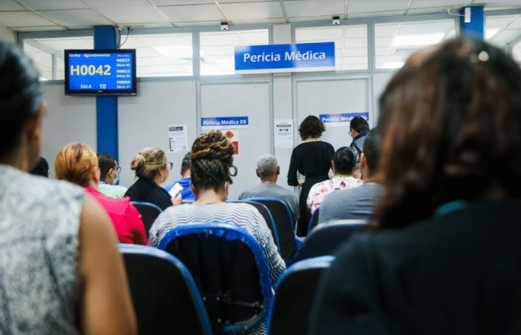 Sala de espera com atendentes e pacientes no INSS, com tela indicando senhas de atendimento