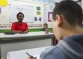 Professora sorrindo na sala de aula durante atividade de avaliação.