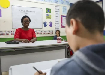 Professora sorrindo na sala de aula durante atividade de avaliação.