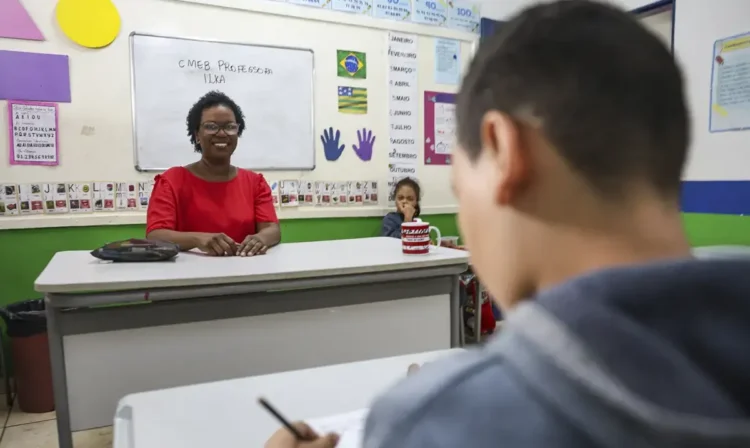 Professora sorrindo na sala de aula durante atividade de avaliação.