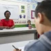 Professora sorrindo na sala de aula durante atividade de avaliação.