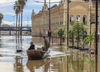 Barco transporta pessoas em rua alagada após enchente em área urbana