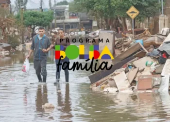 Mulheres e homens caminhando em uma rua inundada, com lixo espalhado ao lado. Logo do programa Bolsa Família visível.