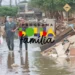 Mulheres e homens caminhando em uma rua inundada, com lixo espalhado ao lado. Logo do programa Bolsa Família visível.