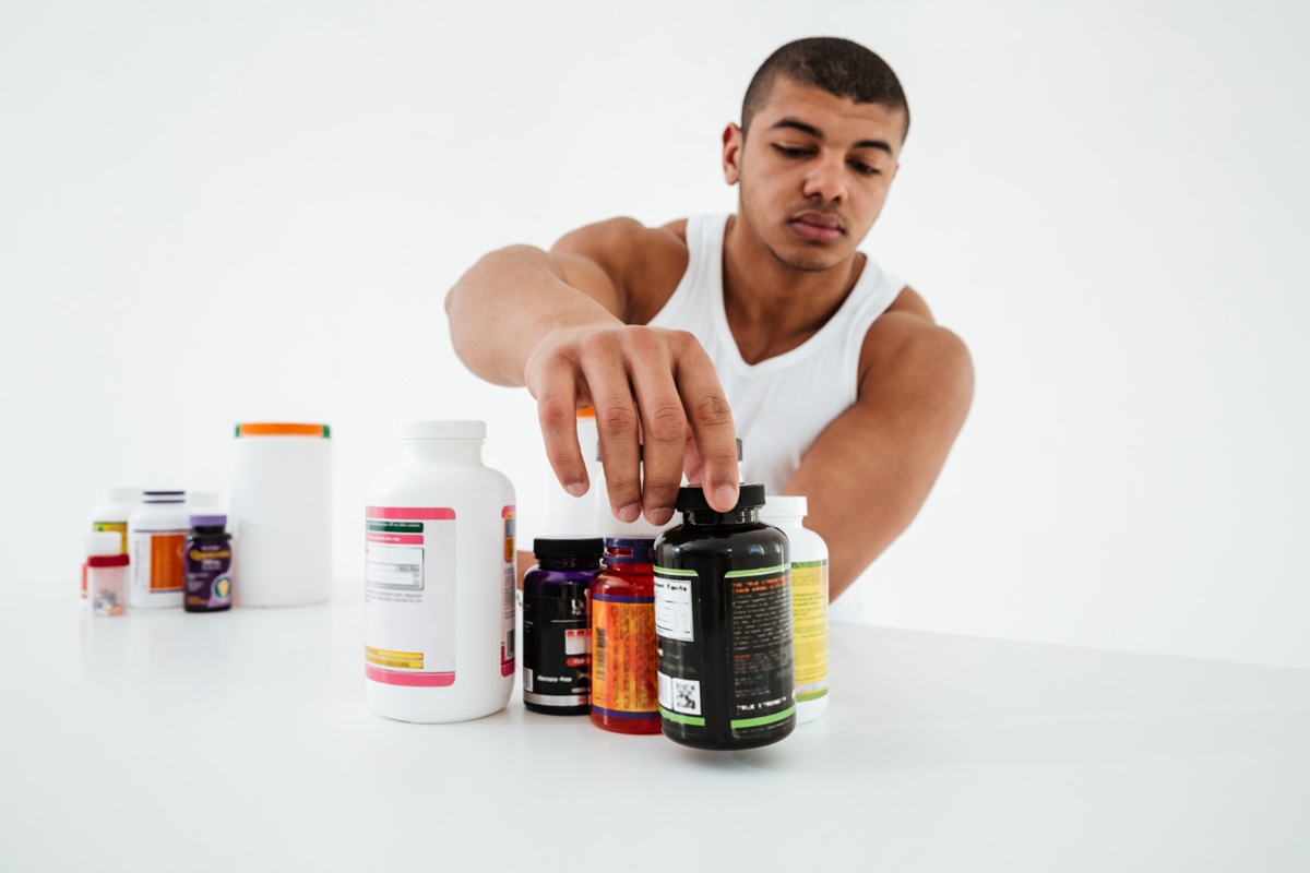 Pessoa pegando frascos de suplementos de uma prateleira, simbolizando a consulta sobre a lista de produtos permitidos.