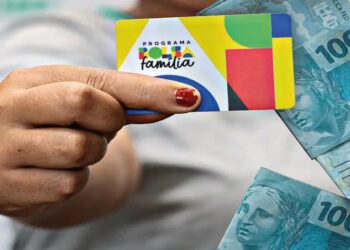 Pessoa segurando o cartão do Bolsa Família ao lado de notas de R$ 100 reais