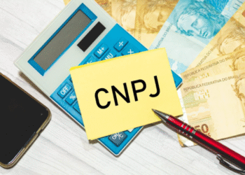 Imagem com calculadora, notas de real e um post-it com a inscrição CNPJ, simbolizando mudanças no registro de empresas.