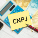 Imagem com calculadora, notas de real e um post-it com a inscrição CNPJ, simbolizando mudanças no registro de empresas.