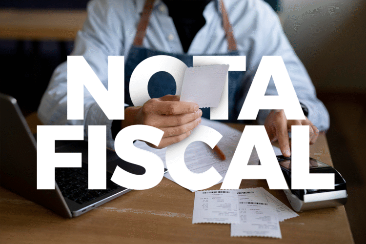 Pessoa segurando nota fiscal com computador e comprovantes sobre a mesa