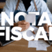 Pessoa segurando nota fiscal com computador e comprovantes sobre a mesa