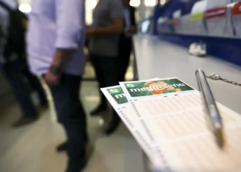 Volantes da Mega-Sena em balcão de lotérica com pessoas ao fundo