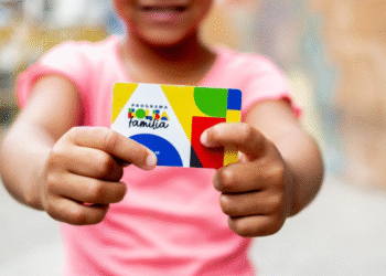 Criança segurando cartão do Programa Bolsa Família com fundo desfocado.