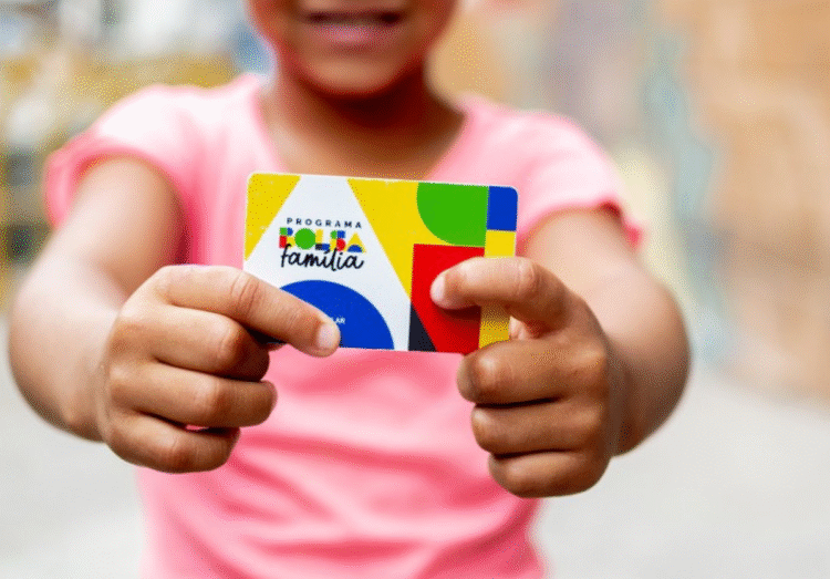 Criança segurando cartão do Programa Bolsa Família com fundo desfocado.