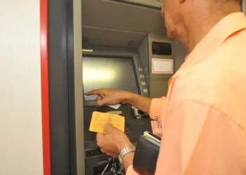 Homem utilizando caixa eletrônico com cartão e extrato em mãos