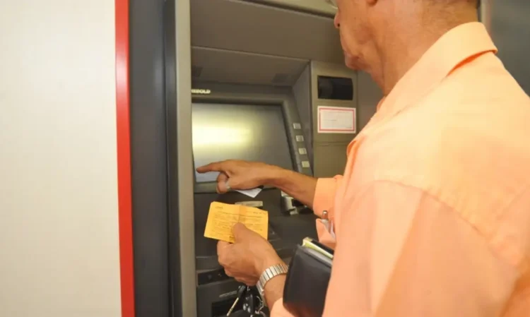 Homem utilizando caixa eletrônico com cartão e extrato em mãos