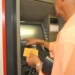 Homem utilizando caixa eletrônico com cartão e extrato em mãos