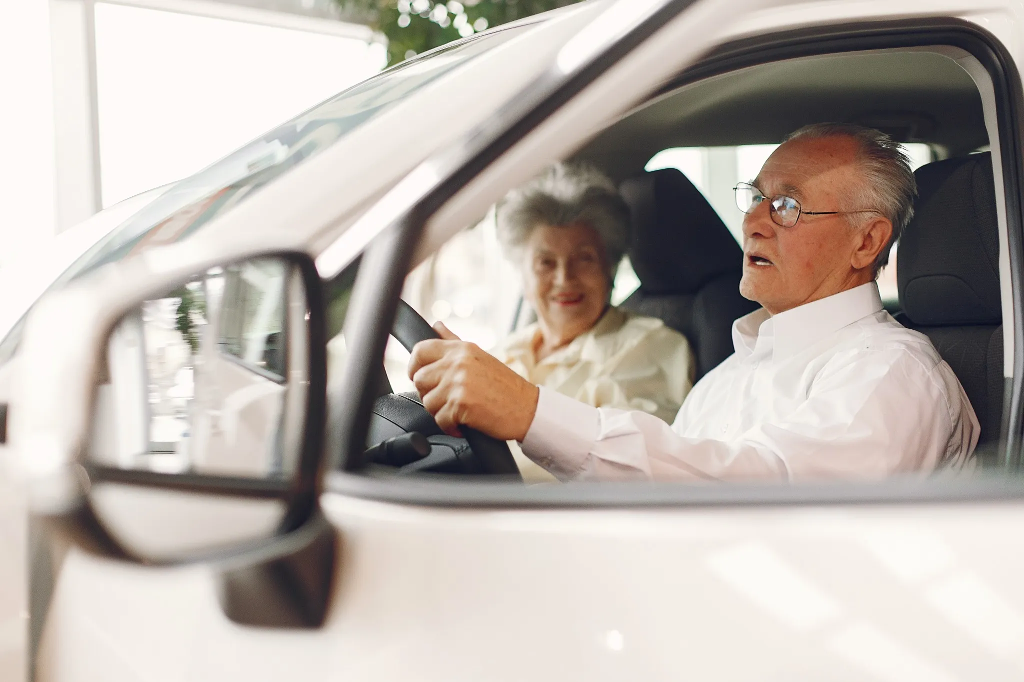 Casal idoso sorrindo enquanto o homem dirige, ilustrando a importância da renovação da CNH para motoristas mais velhos.