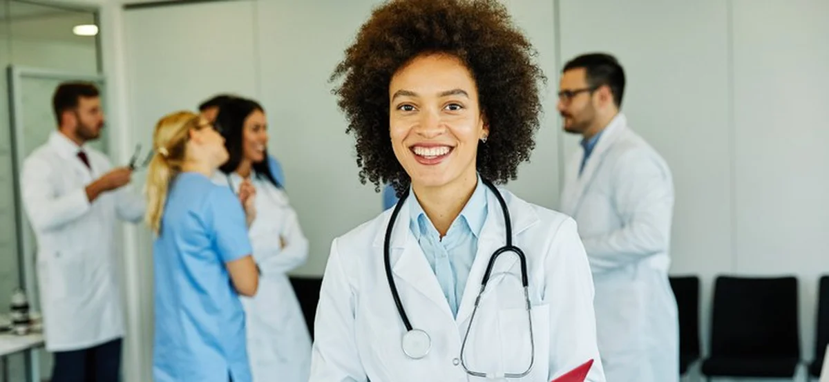 Médica sorridente com equipe de profissionais de saúde ao fundo